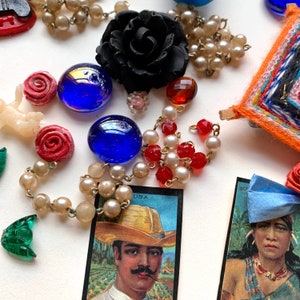 May include: A collection of vintage jewelry and trinkets, including a black rose brooch, red and white beads, blue glass beads, and a small woven tapestry with colorful stripes.