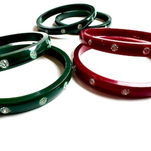 May include: A set of green and red plastic bangles with clear rhinestones. The bangles are stacked on top of each other.