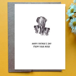 May include: A Father's Day card featuring a watercolor illustration of three elephants, with the adult elephant in front and two smaller elephants behind. The card reads "HAPPY FATHER'S DAY FROM YOUR HERD" in black text on a white background.