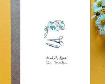 May include: A white greeting card featuring a watercolor illustration of a surgical cap with blue and pink baby footprints, a pair of metal surgical scissors, and a scalpel. Below the illustration, the text reads World's Best! Dr. Madden.