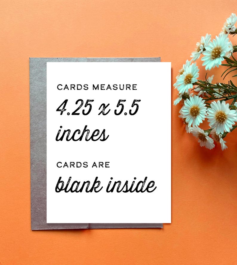 Op de afbeelding: Een witte rechthoekige wenskaart met zwarte tekst die luidt CARDS MEASURE 4.25 x 5.5 inches en CARDS ARE blank inside. De kaart ligt op een grijze envelop tegen een oranje achtergrond, met een bosje witte bloemen ernaast.