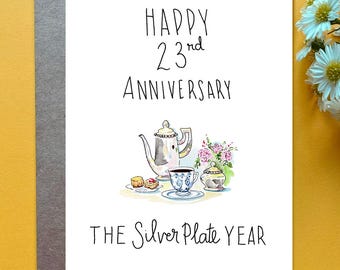 May include: A white greeting card with black handwritten text that reads Happy 23rd Anniversary and The Silver Plate Year. The center features a watercolor illustration of a silver teapot, a teacup, a sugar bowl, and small pastries.