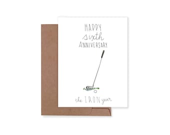 May include: A white greeting card with black hand-lettered text that reads Happy sixth Anniversary and the IRON year. The card features a simple illustration of a golf club resting on a small patch of green grass next to a white golf ball.