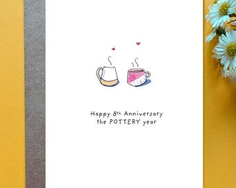 May include: A white greeting card featuring a hand-drawn illustration of two mugs with steam and small red hearts above them. The text reads Happy 8th Anniversary the POTTERY year. The card is placed on a gray envelope against a yellow background.