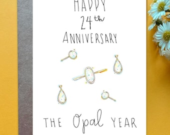 May include: A white greeting card with black handwritten text that reads Happy 24th Anniversary and The Opal Year. The card features colorful hand-drawn illustrations of a ring and four opal-style jewelry pieces scattered across the center.