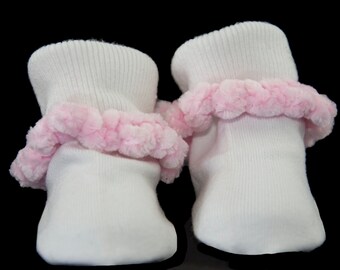 May include: A pair of white baby socks with pink fluffy trim around the top of each sock.