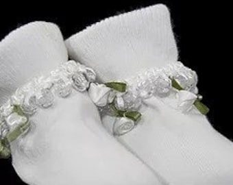 May include: White baby socks with a white lace trim and green ribbon bows.