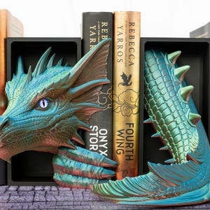 May include: A pair of dragon-themed bookends in shades of teal, blue, and green. One bookend features a dragon's head, the other its tail. Books with gold and black spines are nestled between the bookends. The books have the titles "Fourth Wing", "Onyx Storm", and "Flame".