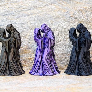 May include: Three figurines of two hooded figures dancing together. The left and right figurines are matte black, while the center figurine is a metallic purple. Each figure wears a long, flowing robe with draped sleeves and a deep, pointed hood.