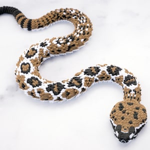 May include: A flexible articulated snake toy featuring a repeating pattern of brown, black, and white segments. The body is constructed from interlocking plastic pieces that allow for movement, ending in a detailed head with black and brown markings.