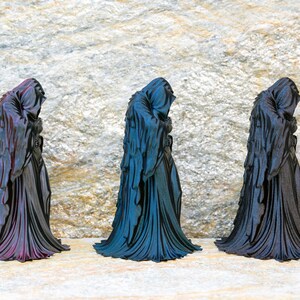 May include: Three standing figurines of hooded figures draped in long, flowing robes. The left figurine features a purple and black iridescent finish, the center one has a blue and black iridescent finish, and the right one is solid matte black.