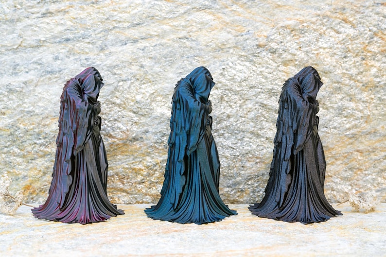 May include: Three standing figurines of hooded figures draped in long, flowing robes. The left figurine features a purple and black iridescent finish, the center one has a blue and black iridescent finish, and the right one is solid matte black.