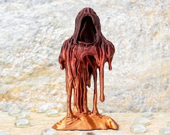 Puede incluir: Una figura impresa en tres dimensiones de una silueta con capucha con un acabado en marrón oscuro y cobre metálico. La capa parece derretirse o gotear, creando largas texturas verticales similares a fluidos que llegan a la base.
