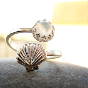 May include: A silver ring featuring a white moonstone and a seashell design. The ring is adjustable and can be worn on any finger.