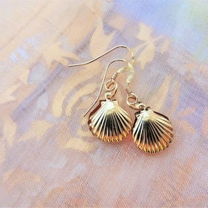 May include: A pair of gold-tone earrings featuring a seashell design. The earrings are dangle style with a hook closure.