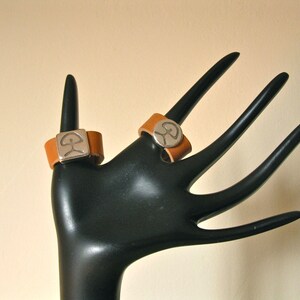 May include: Two brown leather rings with silver metal inlays. The rings feature a stylised tree design.