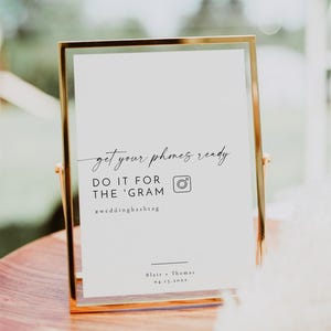 May include: A gold-framed sign with the text "get your phones ready DO IT FOR THE 'GRAM #weddinghashtag Blair + Thomas 04.15.20XX" and an Instagram camera icon.