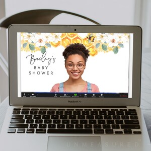 May include: A laptop computer screen displaying a virtual baby shower background with a honeycomb and floral design. The text "Bailey's Baby Shower" is displayed on the screen. A person is visible in the video call window.