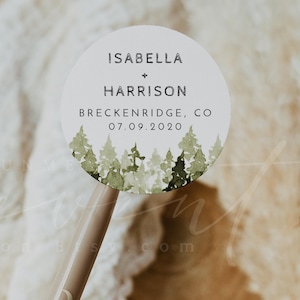 May include: A round white sticker with a watercolor forest design. The sticker says "Isabella + Harrison, Breckenridge, CO 07.09.2020".