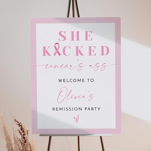 May include: Pink welcome sign with the text "She Kicked Cancer's Ass" and a pink ribbon. The sign also says "Welcome to Olivia's Remission Party" with a pink heart.