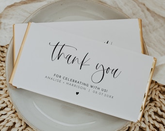 May include: White chocolate bar with gold foil wrapping and a thank you message for celebrating with Analise and Harrison on 08.07.20XX. The bar is on a white plate with a woven straw placemat.