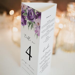 Op de afbeelding: Paarse bloemige bruilofttafelnummer met een zwart nummer 4. De kaart bevat ook de tekst "Table no." en de namen "Jennifer & Lawrence" met de locatie "Telluride, Colorado". De achterkant van de kaart heeft een bruiloftmenu met de koppen "Menu" en "Drinks".