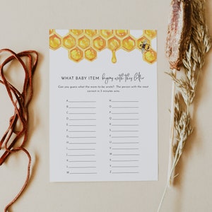 May include: A printable baby shower game with a honeycomb and bee illustration. The game asks guests to write down baby items that start with each letter of the alphabet. The text on the game reads "What baby item begins with this letter?"