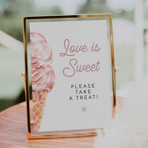 May include: A gold-framed sign with a pink watercolor ice cream cone and the text "Love is Sweet. Please take a treat!"