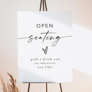 May include: White sign with black text that reads "OPEN seating" with a small heart symbol and the text "grab a drink and sit wherever you like!"