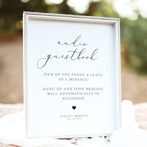 Könnte beinhalten: Ein weißes Schild mit schwarzem Text, auf dem "audio guestbook" steht.  Das Schild fordert die Gäste auf, den Hörer abzunehmen und eine Nachricht zu hinterlassen.  Das Schild gibt auch an, dass die Nachricht automatisch aufgezeichnet wird.  Das Schild ist mit einem kleinen schwarzen Herzen und den Namen "Evelyn + Michael" sowie dem Datum "09.14.20XX" verziert.