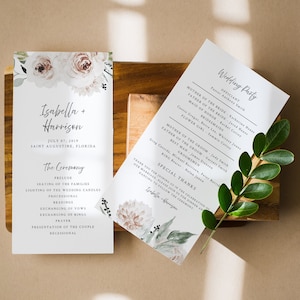 May include: Wedding ceremony program with floral design and text that reads "Isabella + Harrison" and "July 07, 2019" and "Saint Augustine, Florida". The program lists the order of the ceremony, including the prelude, seating of the families, lighting of the wedding candles, processional, readings, exchanging of vows, exchanging of rings, prayer, presentation of the couple, and recessional.