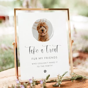 Może przedstawiać: Biały znak z czarnym tekstem, który brzmi "Take a Treat Fur My Friends Who Couldn't Make It To The Pawty!" z symbolem odcisku łapy na dole. Zdjęcie psa rasy golden doodle znajduje się w kółku na górze znaku.