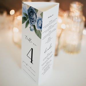 May include: A white wedding table number card with a blue floral design. The card has a black number "4" and the text "Table no." The card also includes the text "Jennifer & Brandon" and the date of the wedding.