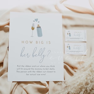 May include: A white card with blue text that says "How big is her belly?" with a blue illustration of a bottle and a champagne glass. The card is on a light pink surface with a white fluffy plant.