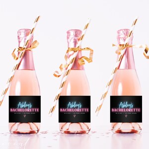 Può includere: Tre mini bottiglie di champagne con etichette rosa su cui è scritto "Ashley's Bachelorette" in rosa neon. Ogni bottiglia ha una cannuccia a strisce bianche e dorate e un nastro dorato legato intorno al collo.