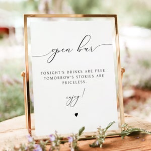 May include: A gold-framed sign with the text "open bar" in a cursive font. The sign also includes the text "Tonight's drinks are free. Tomorrow's stories are priceless. enjoy!" with a small black heart at the bottom.