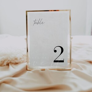 May include: A gold-framed table number sign with the word "table" and the number "2" in black text on a white background.