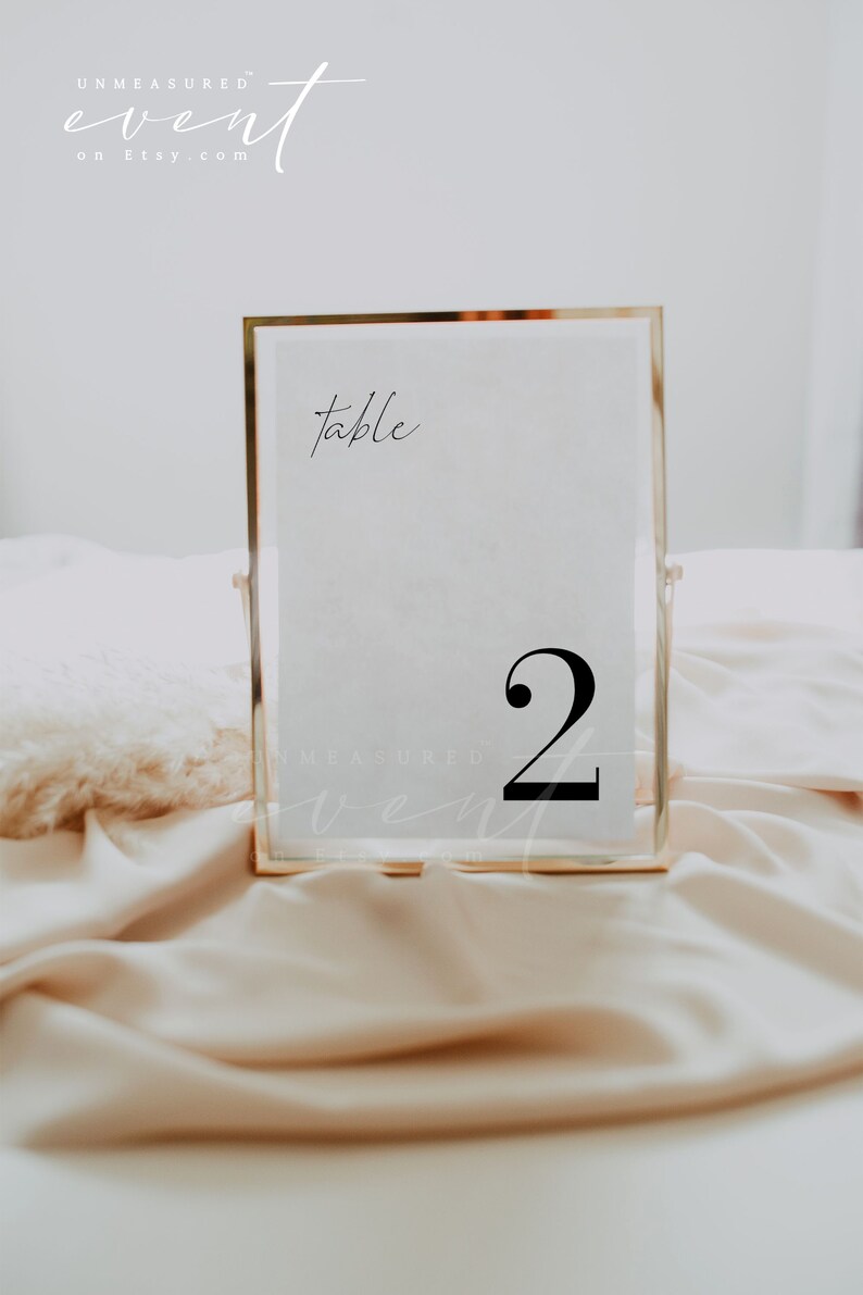 May include: A gold-framed table number sign with the word "table" and the number "2" in black text on a white background.