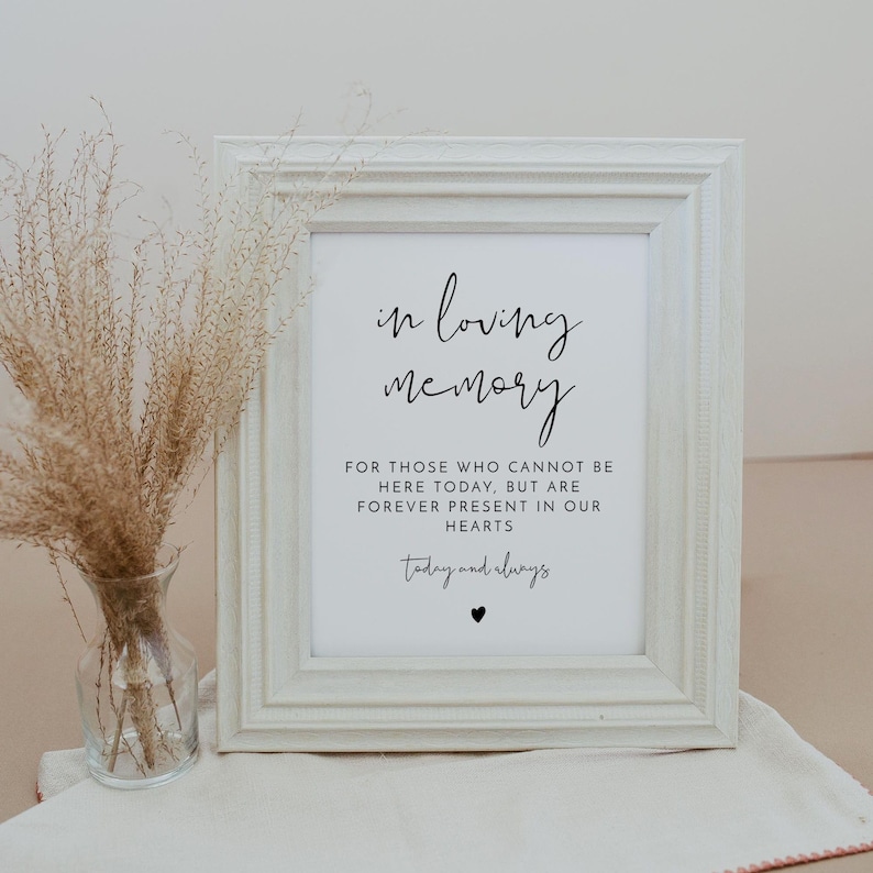 K&ouml;nnte beinhalten: Ein wei&szlig; gerahmtes Schild mit schwarzem Text, der "in loving memory" und "For those who cannot be here today, but are forever present in our hearts" und "today and always" mit einem kleinen schwarzen Herzen lautet.