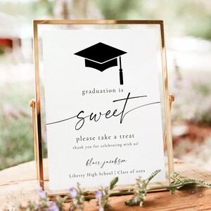 May include: A framed graduation sign with a gold-colored frame. The sign reads "graduation is sweet" with a black mortarboard graphic. The text below says "please take a treat" and includes a name and school.