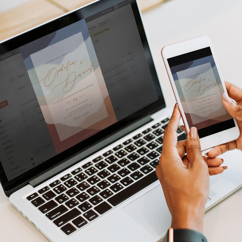 May include: A laptop screen displays a wedding invitation with a watercolor background and the text "Together with their families, Ophelia + Daniel, invite you to celebrate their marriage, 2023". A person is holding a smartphone displaying the same invitation.