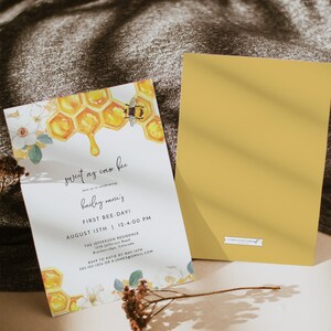 May include: A white invitation card with a watercolor illustration of a honeycomb and a bee. The text on the card reads "sweet as can bee" and "hailey marie's first bee-day!" with the date and time of the event. The card is on a brown textured surface.