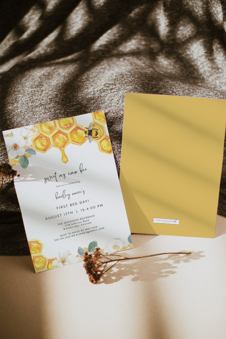 May include: A white invitation card with a watercolor illustration of a honeycomb and a bee. The text on the card reads "sweet as can bee" and "hailey marie's first bee-day!" with the date and time of the event. The card is on a brown textured surface.