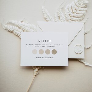 Puede incluir: Un conjunto de invitaciones de boda con una tarjeta blanca que muestra "ATTIRE" y una paleta de colores, un sobre con un sello de cera y hojas de helecho blancas. El texto de la tarjeta pide a los invitados que usen ciertos colores.