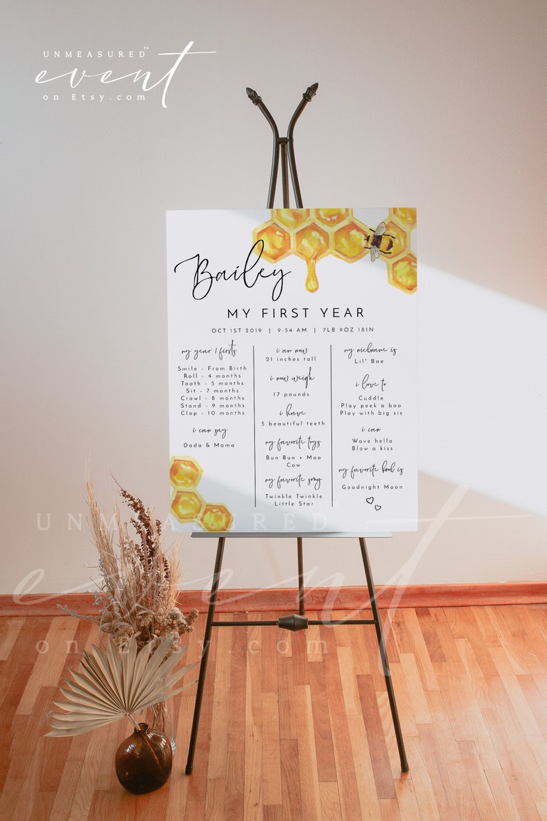 May include: A white poster with a honey comb design and a bee. The poster is titled "Bailey My First Year" and includes details about Bailey's first year of life, including birth date, weight, height, and milestones.