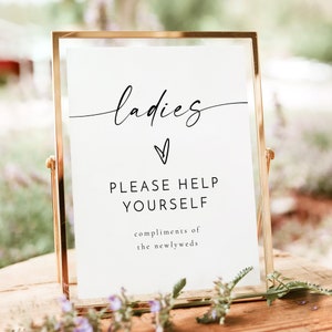 May include: A gold-framed sign with white background and black text that reads "ladies" with a heart symbol and "PLEASE HELP YOURSELF compliments of the newlyweds".