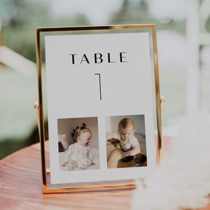May include: A gold-framed table number sign with the text "TABLE 1" and two photos of babies. The photos are in black and white.