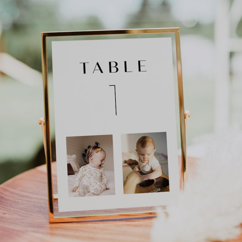 May include: A gold-framed table number sign with the text "TABLE 1" and two photos of babies. The photos are in black and white.