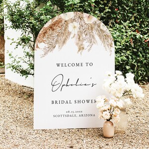 May include: A white welcome sign with a floral design at the top. The sign reads "Welcome to Ophelia's Bridal Shower 08.15.20XX Scottsdale, Arizona".
