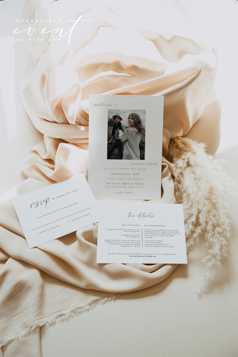 May include: A white wedding invitation with a photo of the couple in the top right corner. The invitation includes the couple's names, wedding date, and location. The text "rsvp by August 20, 20XX" is written in cursive on a separate white card. The invitation also includes a section titled "the details" with information about the reception and accommodations.